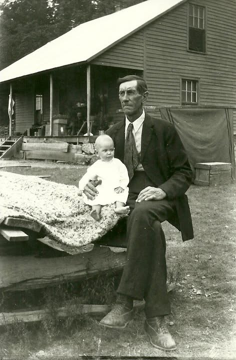 Charles Hubbard Sanders seated outdoors holding a baby, Bernice.